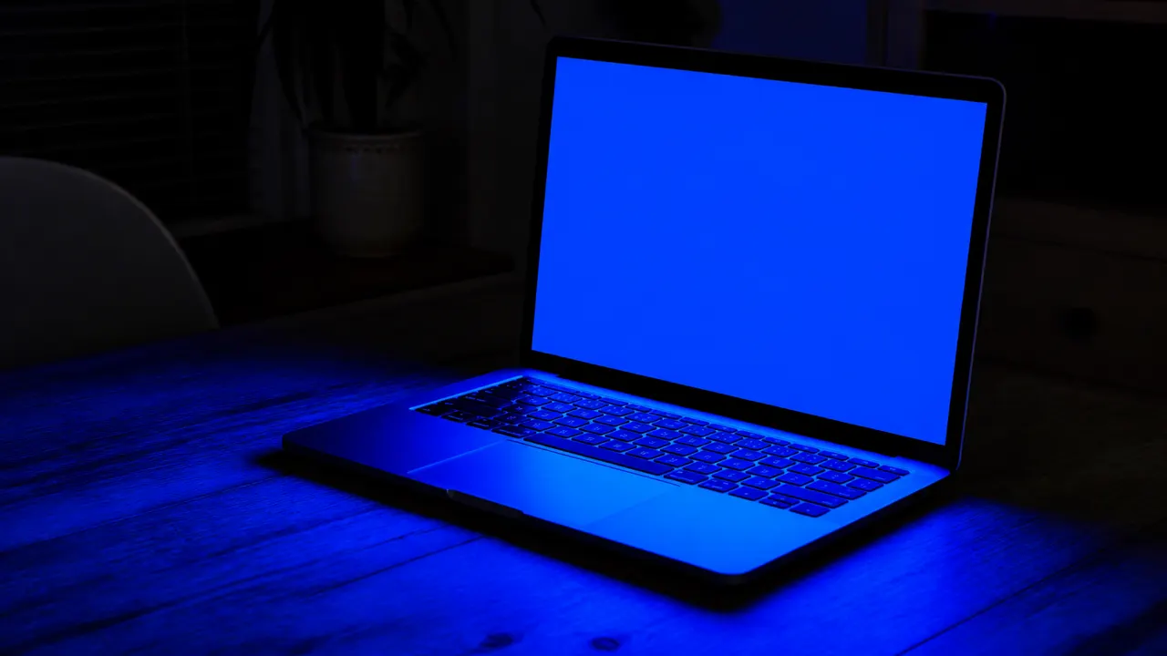 Laptop in a dim room filling the desk with a solid blue glow, no letters or logos