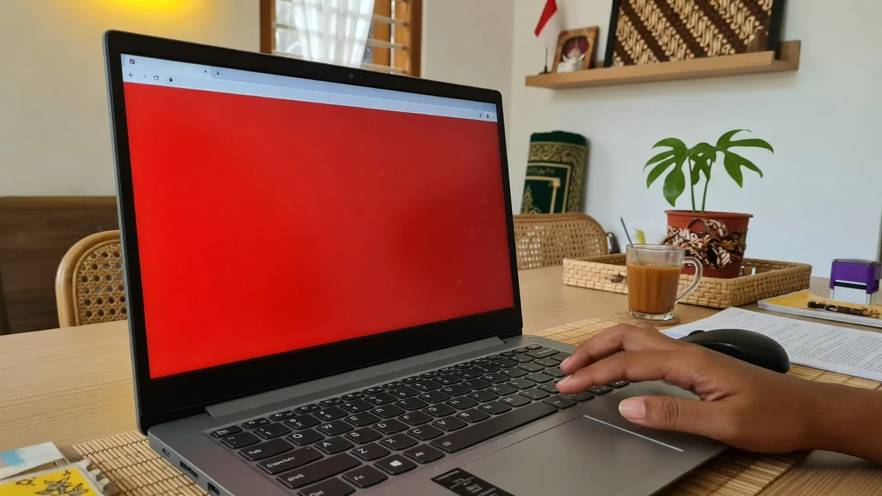 Laptop menampilkan red screen full screen di meja kerja