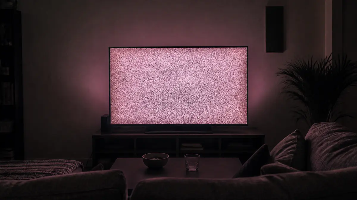 A living-room television filling a dark couch with a soft dusty-rose snow glow, no interface labels. Pink noise here is static plus a balanced hiss in this tab, not a solid pink page.