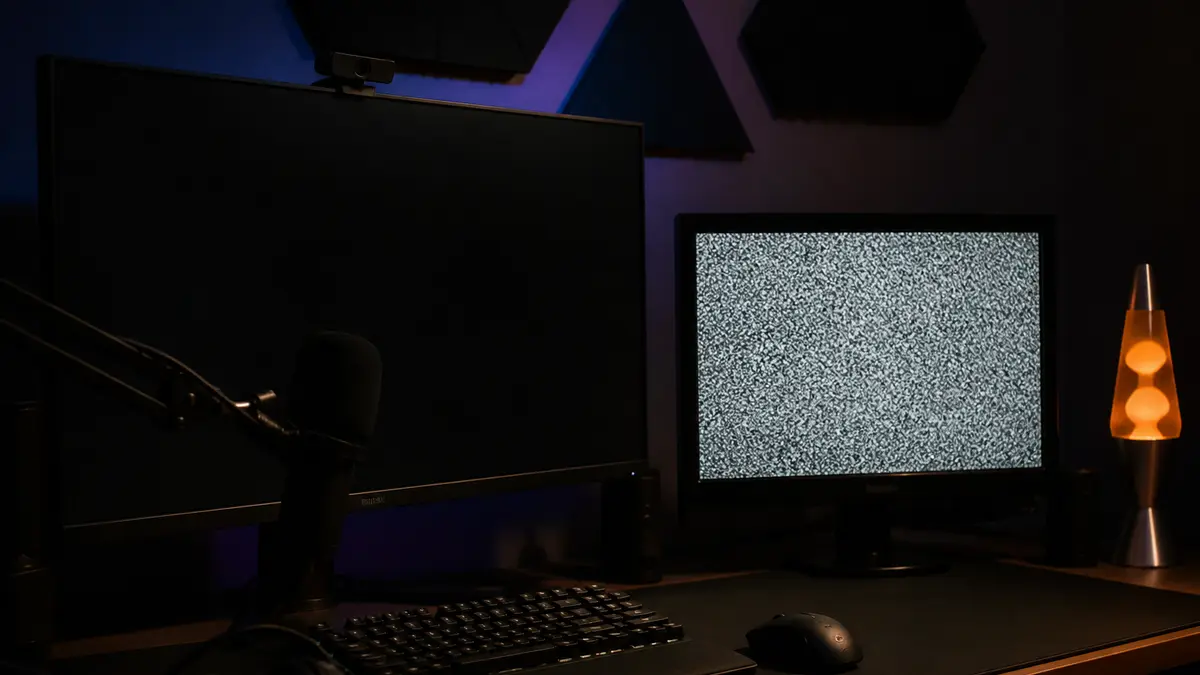 Yayın masasında iki monitör, biri taneli TV karı, arayüz yok. Sessiz ara sahne için tarayıcı penceresini yakala.