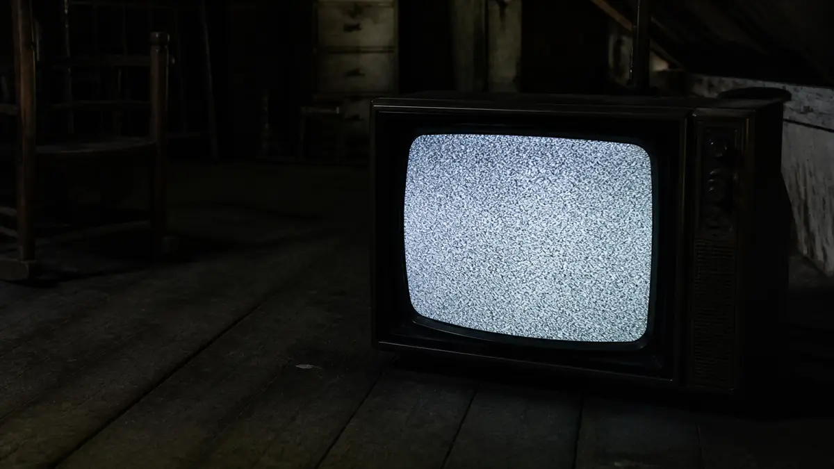 Loş çatı katında taneli analog kar gösteren eski CRT, harf veya logo yok. Retro ve korku kesmesi aynı sessiz karı kullanır.