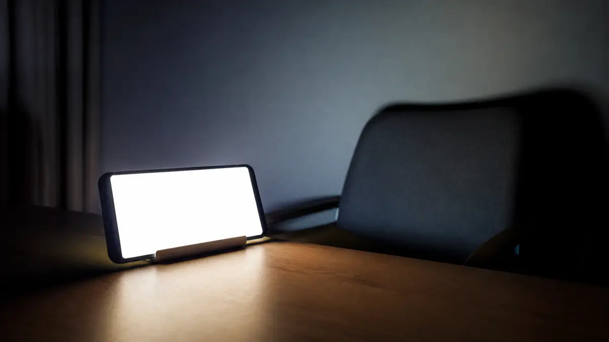 A landscape phone on a stand at night, the screen a solid white glow lighting an empty chair. Native fullscreen is often blocked on phones, so this stopwatch falls back to a layout that still covers the viewport.